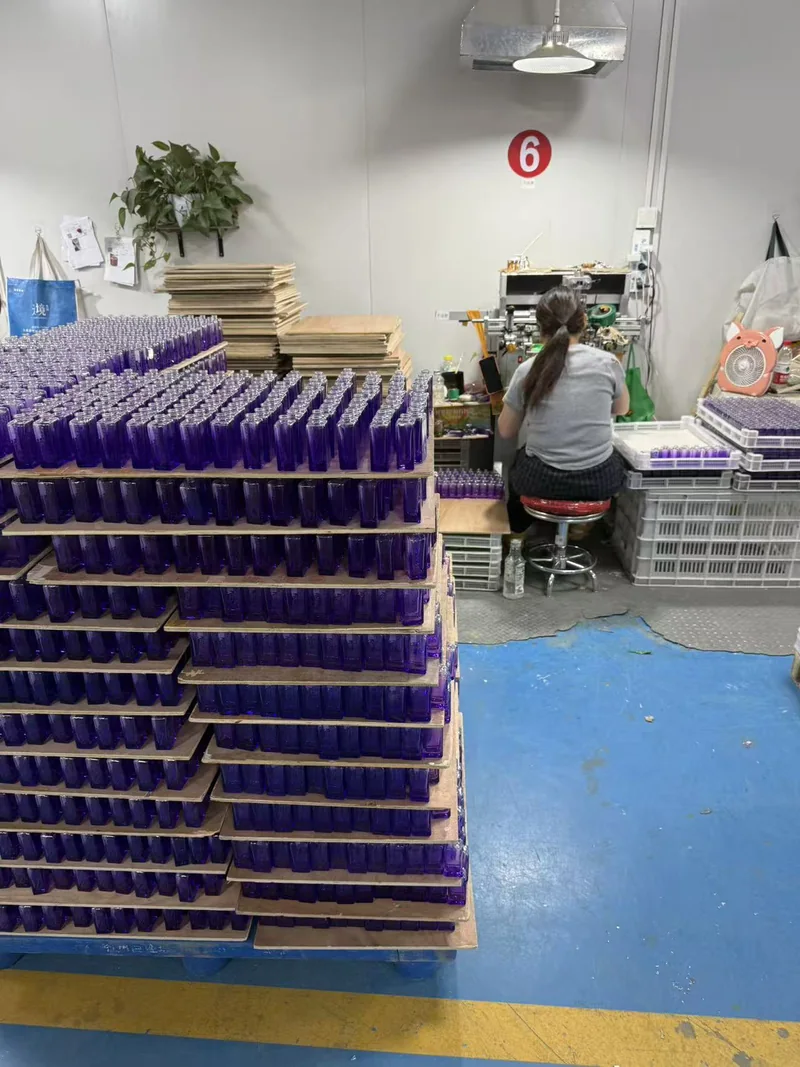 Violett beschichtete Glasflaschen mit Diffusor neben einem Mitarbeiter an der Dekorationsstation